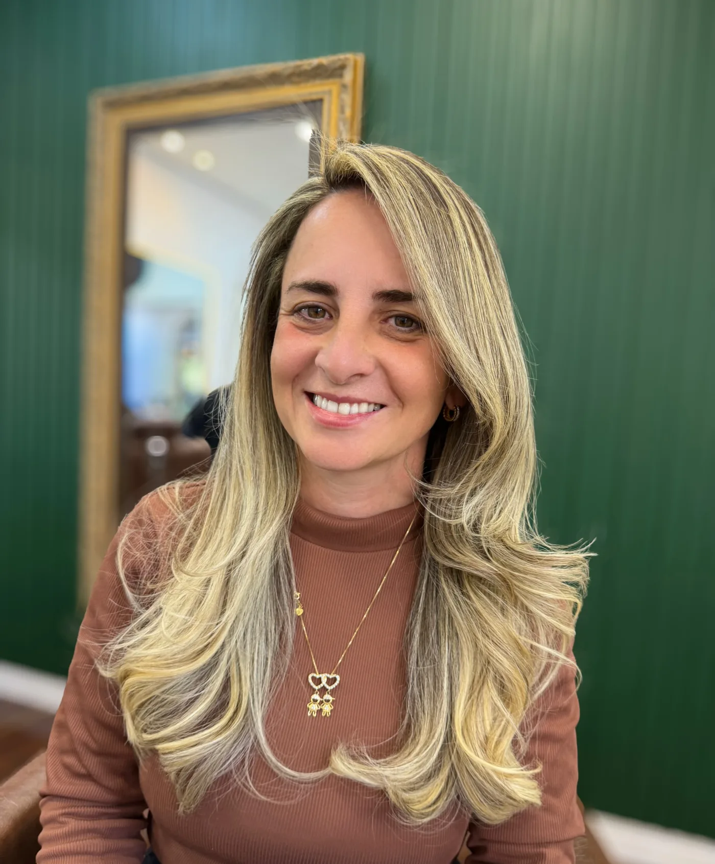 Cliente sorrindo com o cabelo loiro pronto, na parede verde do salão